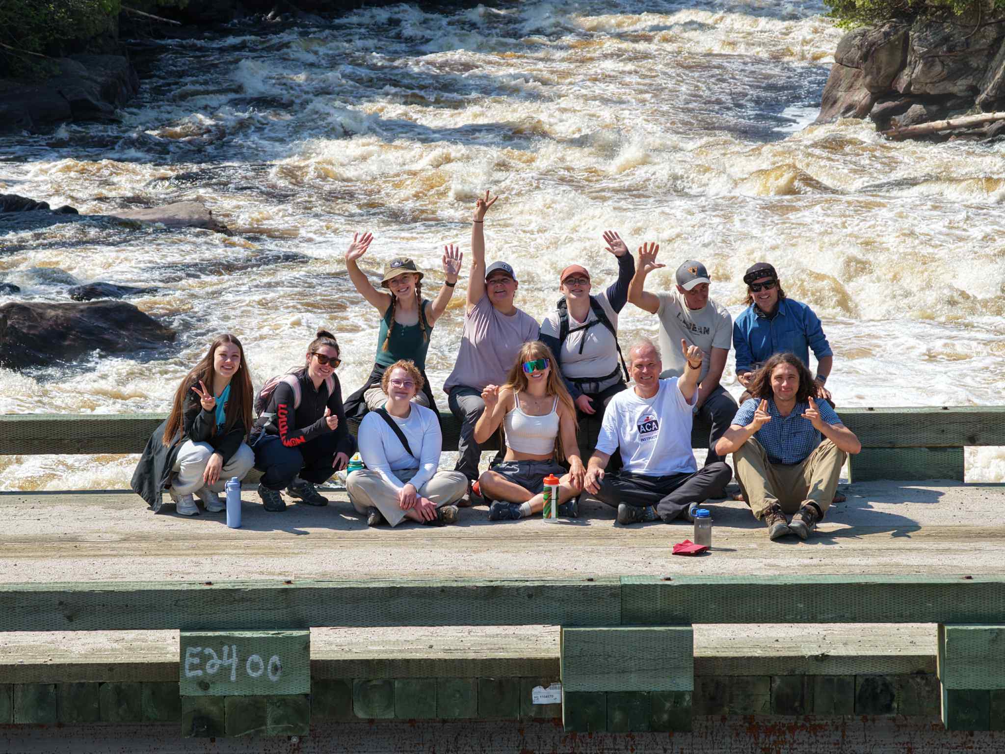 A group of youth and CPAWS staff pose for a photo standing on a bridge overlooking turbulent rapids below.